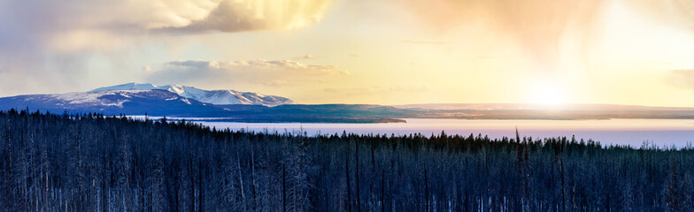 Panoramic frozen winter landscape view of Yellowstone National Park with sunlight shining in the background of the snowy mountain range