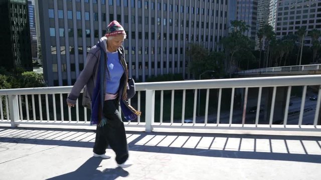 Elderly homeless woman walks on a sidewalk downtown.