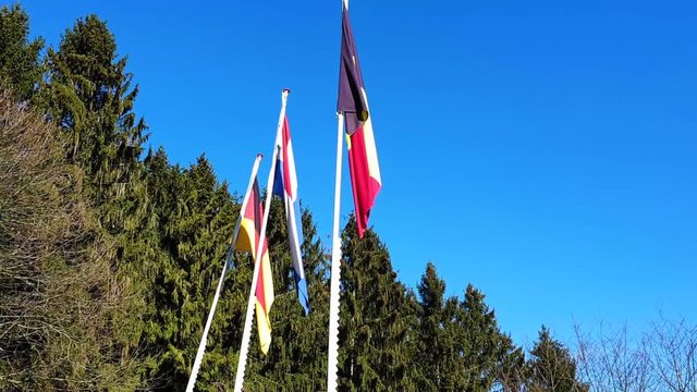 Three Flags (Germany, Netherland & Belgium) raising up in the Sky - Sunny WinterDay