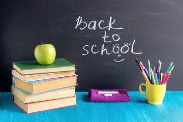 Text Back to school and pupils workplace. Books stationery apple chalk on blue table on background black chalkboard Concept Education