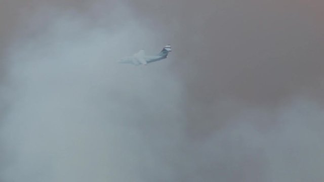 Jumbo fire bomber flying through smoke of massive wild fire.