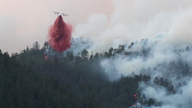 Jumbo fire bomber flying through smoke of massive wild fire to drop slurry.