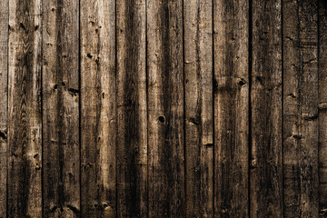 A wall made of old, dark, worn brown wooden knotty planks