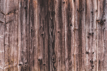 Background from old worn, darkened from time to time, brown knotty vertical wooden plank close up