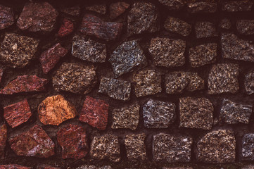 An old darkened from time to time wall with granite roughly treated stones of red gray and yellow shades