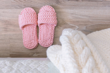 Fototapeta na wymiar Cozy pink knitted slippers beside the bed. Bedroom. White knitted blanket on the bed.
