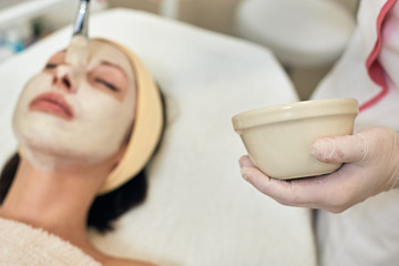 Closeup photo of professional beautician applying peeling scrub on female face