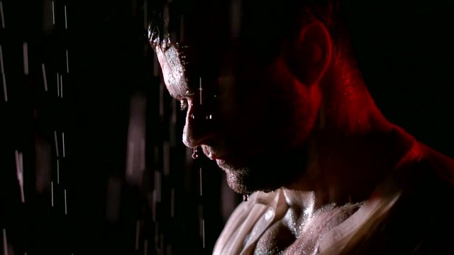 Close-up portrait of a sad man slowly turning his head to camera standing in the rain, studio shoot.