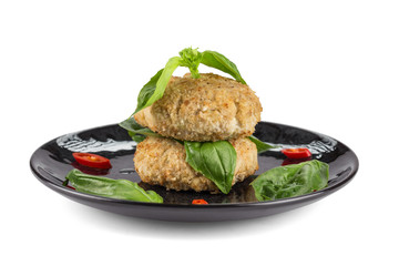 Steamed chicken patties in breaded, served with spinach leaves on a black plate, isolated on a white background with shadows. Dietary food. Close up.