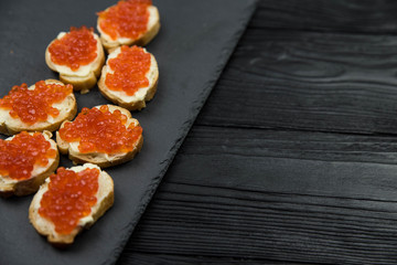 Sandwich from white baguette bread with red salmon caviar on black plate. Russian seafood cuisine. Concept of wealth and riches. 