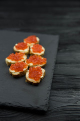 Sandwich from white baguette bread with red salmon caviar on black plate. Russian seafood cuisine. Concept of wealth and riches. 