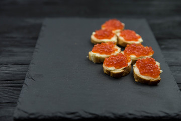 Sandwich from white baguette bread with red salmon caviar on black plate. Russian seafood cuisine. Concept of wealth and riches. 