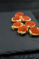 Sandwich from white baguette bread with red salmon caviar on black plate. Russian seafood cuisine. Concept of wealth and riches. 