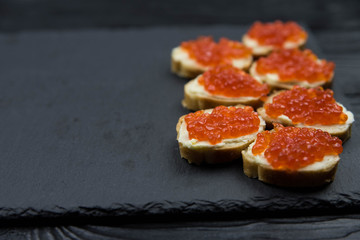 Sandwich from white baguette bread with red salmon caviar on black plate. Russian seafood cuisine. Concept of wealth and riches. 