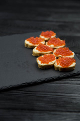Sandwich from white baguette bread with red salmon caviar on black plate. Russian seafood cuisine. Concept of wealth and riches. 