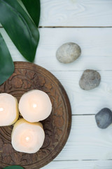 Fototapeta na wymiar White candles, green leaves and grey stones. Concept of harmony, balance and meditation, spa, massage, relax.
