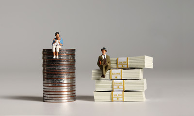 A pile of bills and coins. Miniature people. The concept of pay discrimination for women with...