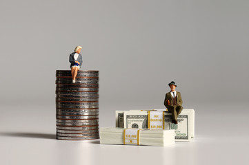 A pile of bills and coins. Miniature people. The concept of inequality in wages for men and women.