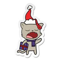 sticker cartoon of a cat with christmas present wearing santa hat