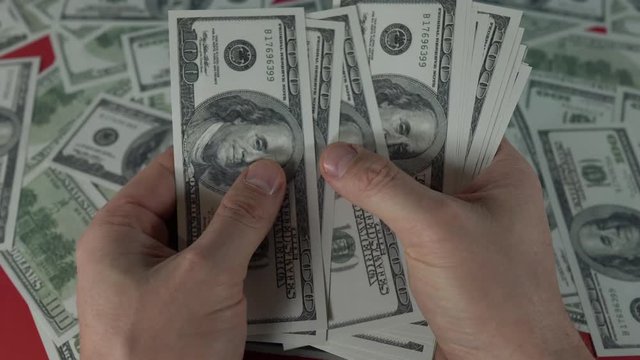 Slow panning shot of male hands slowly counting a stack of money in front of a red table with hundreds of US Dollars on it