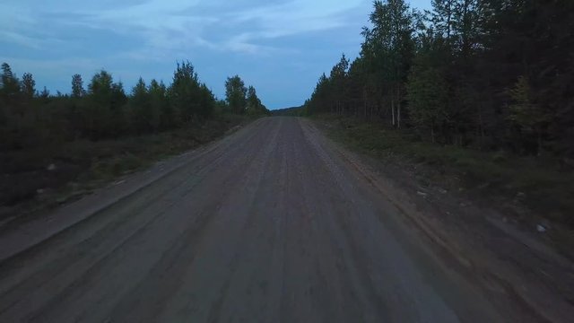 Fast moving drivers point of view driving on gravel road in dusk, forest on both sides of the road, dolly aerial shot, adveture and driving concept, natural landscape of Scandinavia