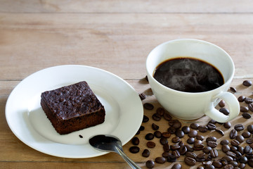 Brownie cake in white dish and black coffee in cup on wooden table