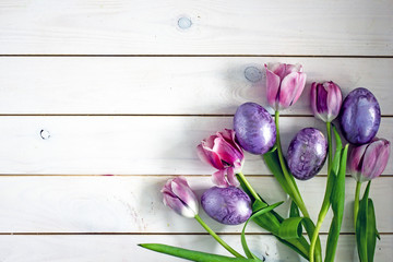  Background for Easter. Flowers tulips and painted Easter eggs of violet color on white wooden background. View from above, copy space