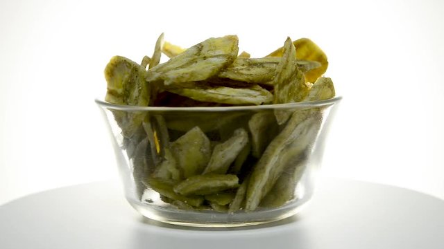 Glass bowl with banana chips rotating on a white background. Flat plane. Eye level