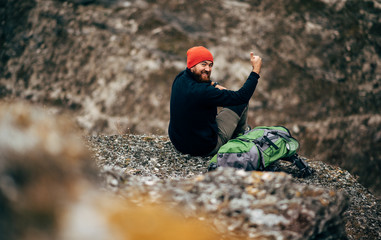 Overhead view image of young man relaxing in mountains after hiking. Rear view of traveler man in red hat, sitting alone have a break after mountaineering. Travel and lifestyle concept