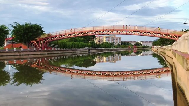 People Commuting Across The River By Modern Design Bridge With Calming Water Reflection View In The Morning