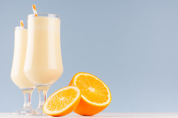 Joyful colorful milk oranges dessert with juicy slices, striped straw on modern elegant blue color background.