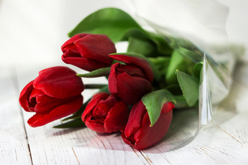 Red tulips in plastic packaging on white wooden background, beautiful spring flowers
