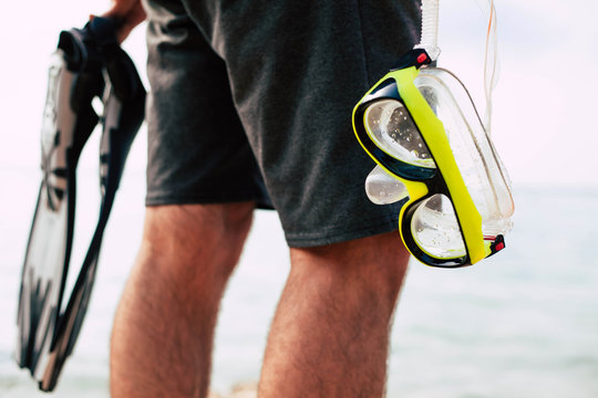 A neon yellow snorkel and grey paddles in the hands of the man wearing black swimming trunks and getting ready to observe the marine life.