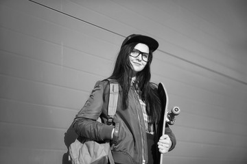 Naklejka premium A young hipster girl is riding a skateboard. Girls girlfriends for a walk in the city with a skateboard. Spring sports on the street with a skateboard.