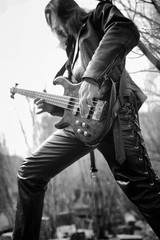Fototapeta na wymiar Rock guitarist outdoor. A musician with a bass guitar in a leather suit. Metalist with a guitar on the background of industrial steps.