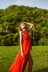 girl in a red dress straightens her long hair against the background of tropical palm trees