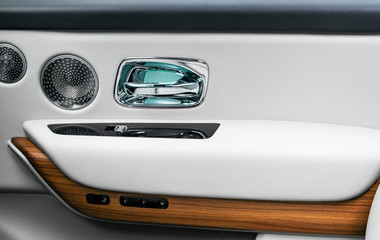 Door handle with power window control buttons of a luxury passenger car. White perforated leather interior with stitching and natural wood panel. Modern car interior details. Car detailing. Car inside