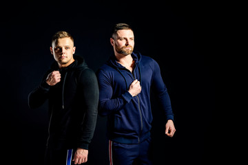 Brutal athletic guys in sport suits looking away on black background