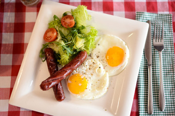 Eggs, salad and sausages on plate on table in cafe
