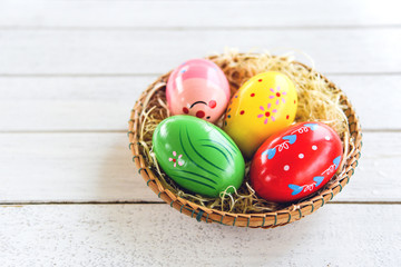 Colorful easter eggs in basket nest decoration on white wooden background