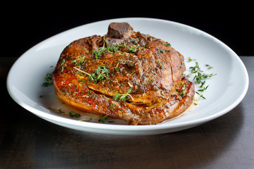 Roast pork knuckle on white plate, sprinkled with rosemary.