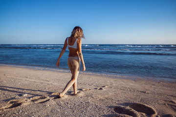 Girl in swimsuit walking on the beach, tanned legs and ass in the sand