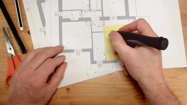 top view, the hand of an interior designer attacks a yellow post on a technical drawing and writes home sale with a pen, ideal footage for topics such as building renovation