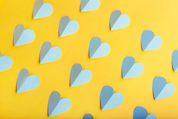Fototapeta na wymiar Flat lay of blue paper hearts in rows on yellow background