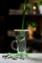 Expert barman making cocktail at nightclub. Bartender preparing green cocktail at cocktail glass at the bar. Preparing of green cosmopolitan cocktail. Green alcoholic drink in glasses on bar.