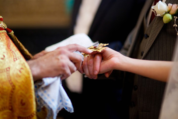 Hands of the newlyweds and the priest's cross at the wedding in the Church