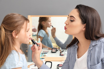 Young mother applying lipstick onto daughter's lips at home