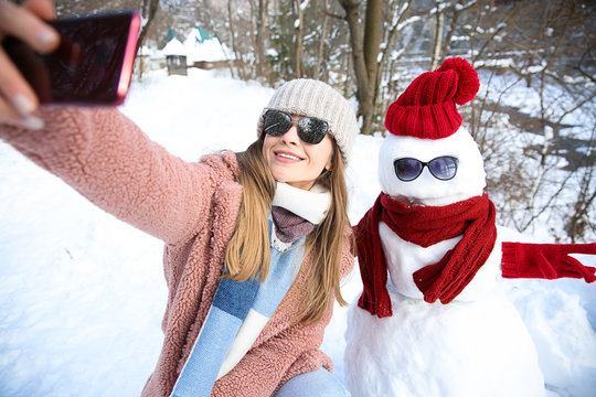 Happy woman taking selfie with snowman on winter day