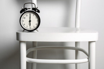 Alarm clock on chair against white background