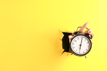 Female hand with alarm clock visible through hole in torn color paper